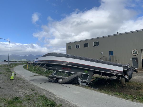 A outboard boat is upside down next to a large cargo facility.