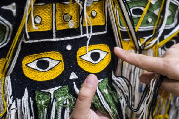 A yellow and black woven robe with Northwest Coast art motifs. The artist's hands are pointing at the design.