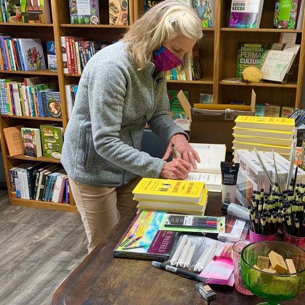 Author in a mask signing books with yellow covers.