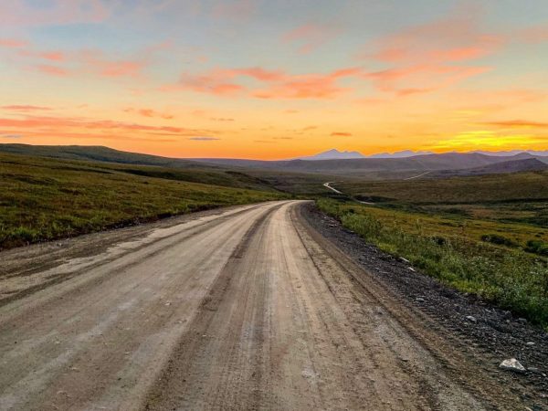 A dirt road leads into rolling mountains in a sunset