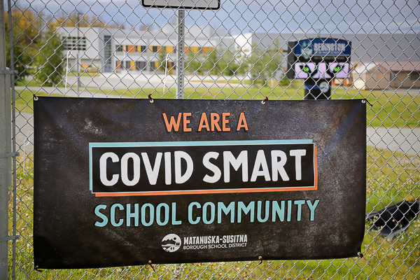 a banner hung on a fence that reads "we are a covid smart school community"