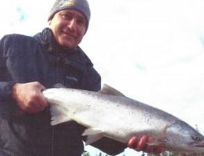 A man in a beanie and a black coat holds a salmon
