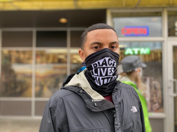 A portrait of a young Black man wearing a mask that says "Black Lives Matter"