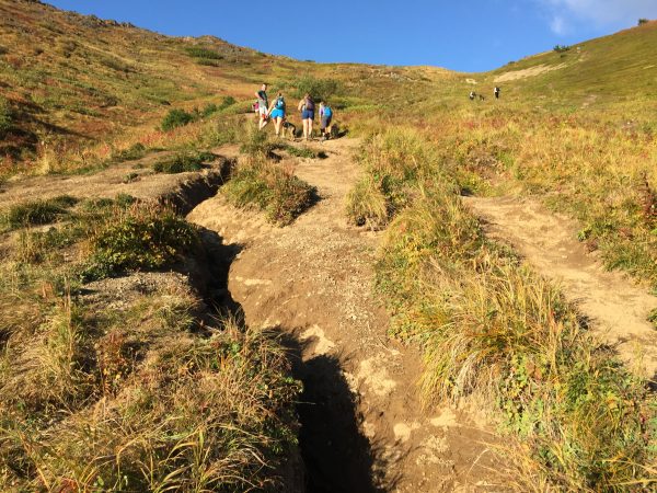 Ruts in the dirt lead up a mountain where hikers are visible