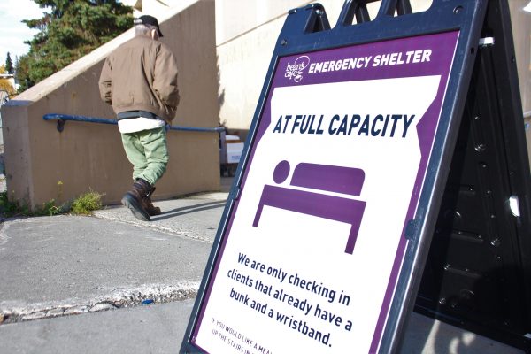 A purple fold-out sign with the words "Full Capacity". Behind it, a man in a tan jacket descends a ramp