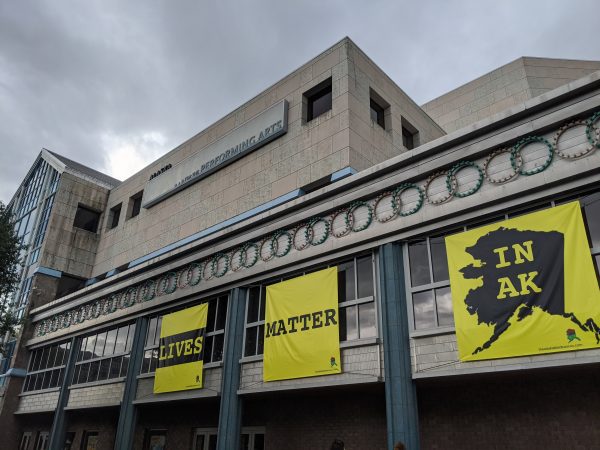 Three yellow banners affixed to the side of the building that read "Lives," "Matter," and "In AK"