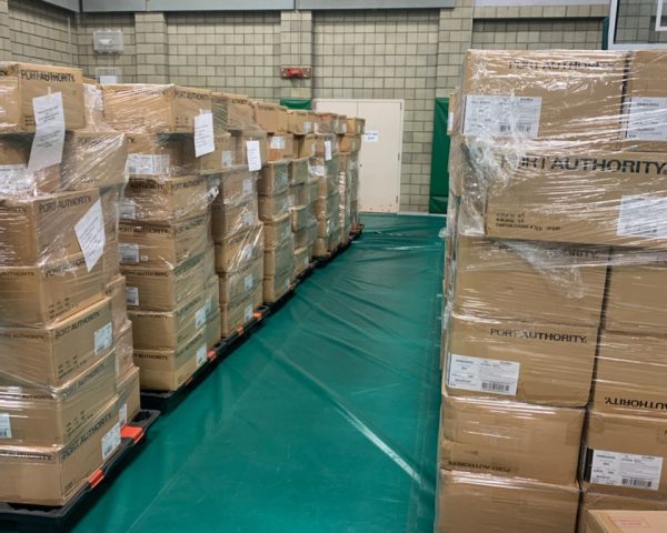 Dozens of cardboard boxes containing cloth masks are stacked on pallets inside a warehouse.