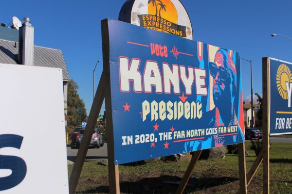 A Kanye sign next to two other political signs with a sign for Espresso Expressions in the background