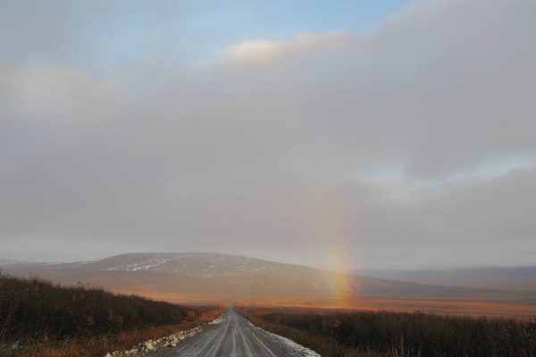 A rainbow above a gravel road with mountains in the background