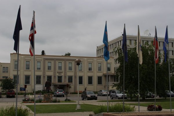 A beige blocky building with a parking lot in front and a half dozen flags 