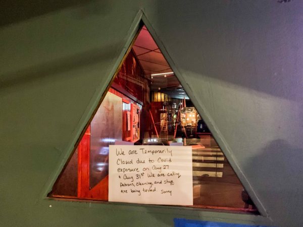 A triangular window into a bar with a sign posted outside about a closure. 