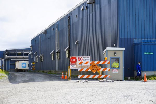 A blue warehouse building with a small entry building oustdie where employees in hazmat equiipment wait