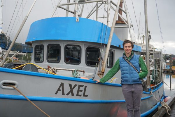 A woman stands to the side of a fishing boat named Axel leaning with her hand on the boat