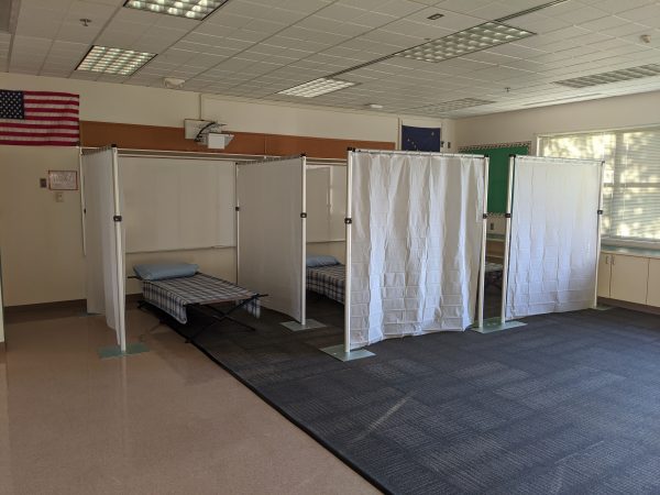 An empty room with three cots that have a pillow and blanket on them each separated by white curtains.