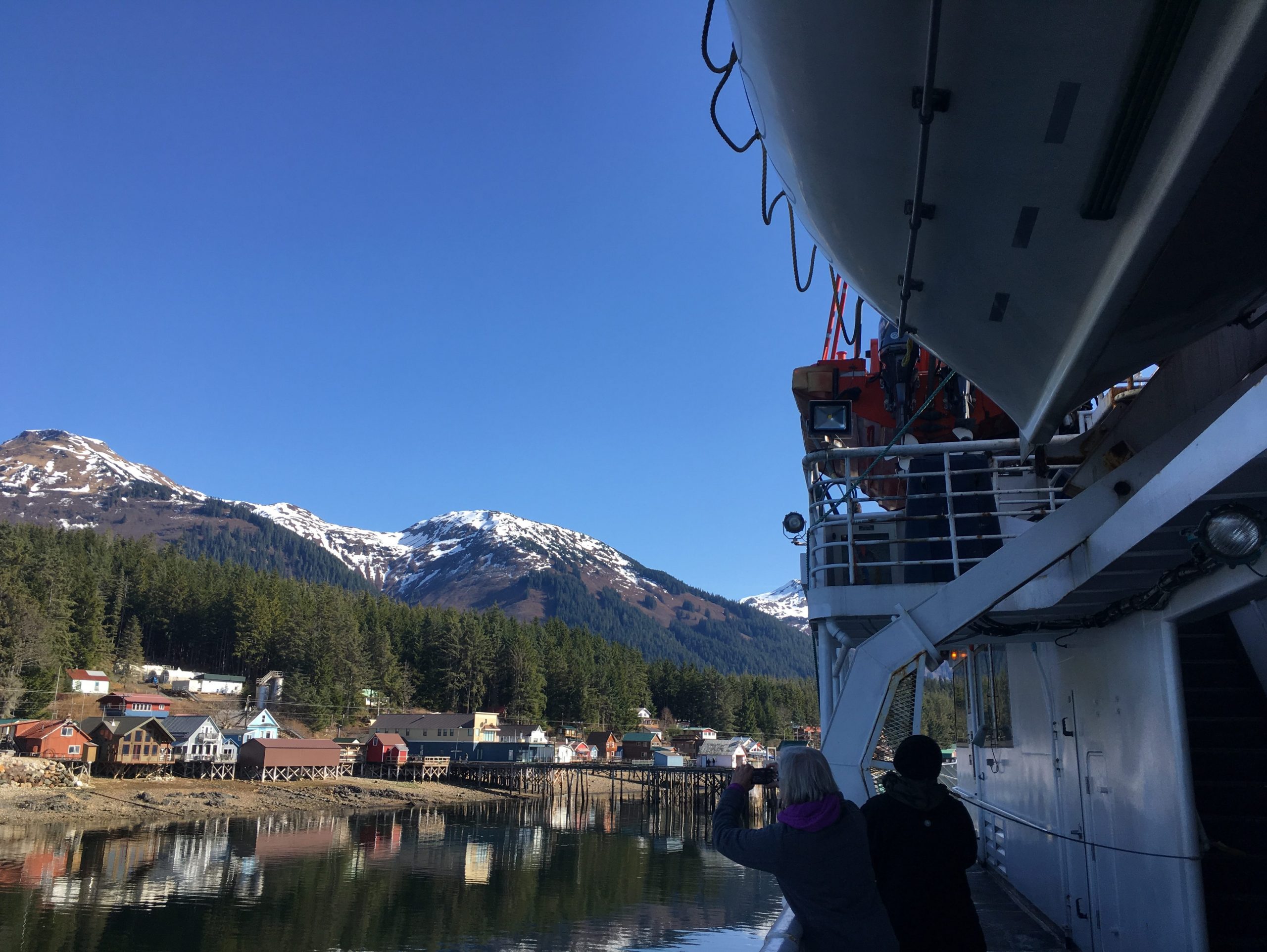 A ferry approaches a town next to spruce covered mountains