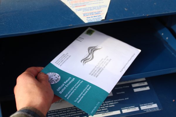 An envelope with a division of elections address is placed in a mailbox