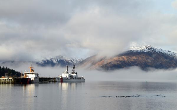 A coast guard cutter mooring at a dock with mountains in the background