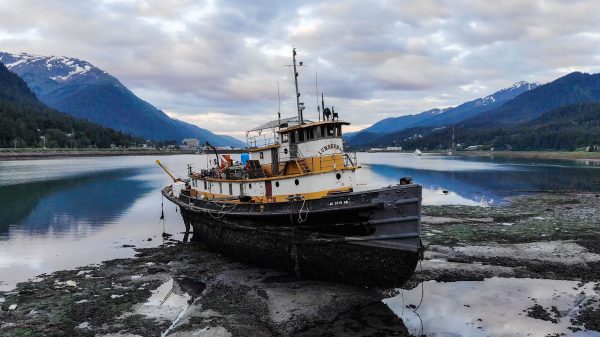 A weathered greyissh tugboat on the sandy beach with mountains in the background