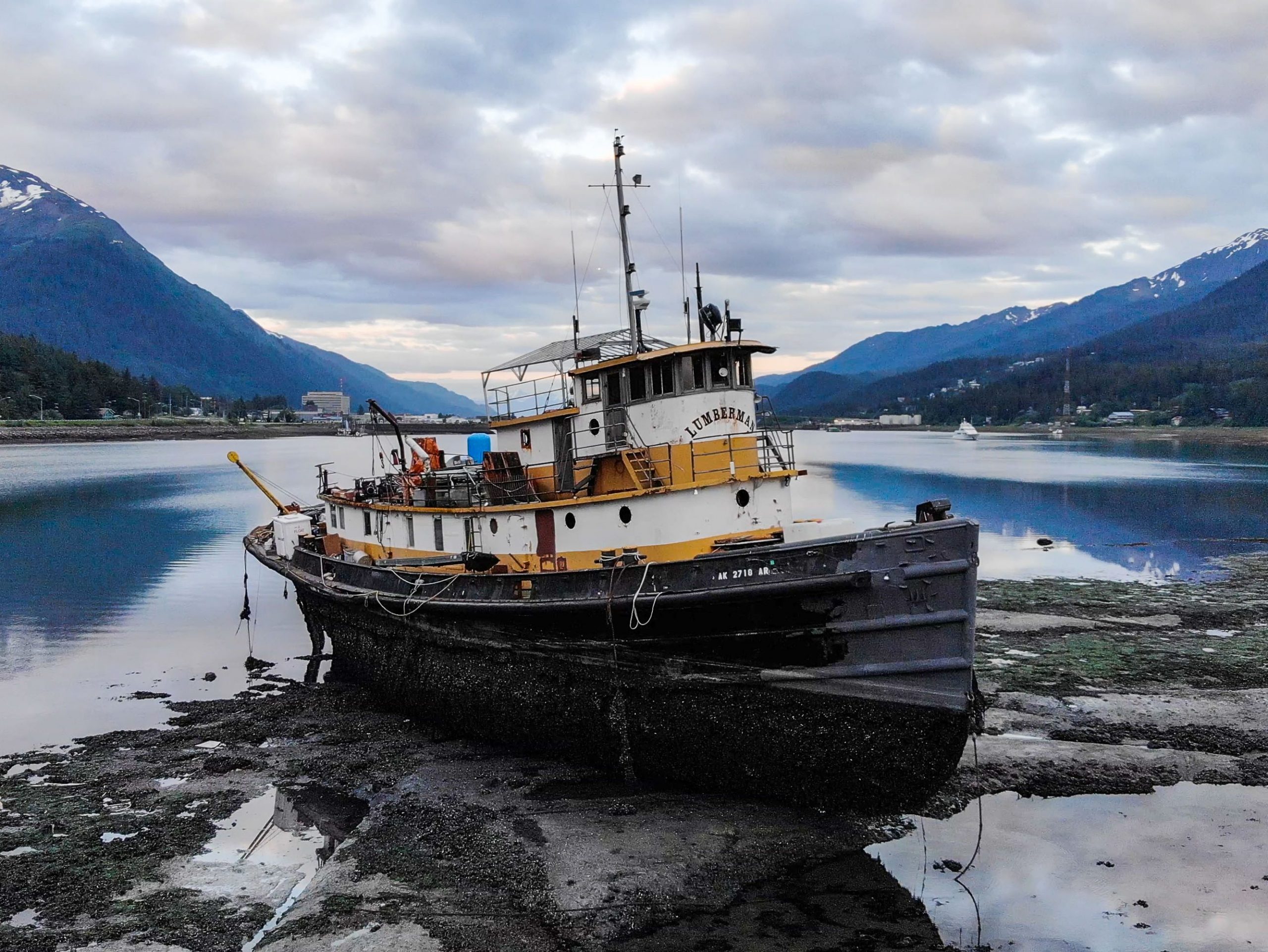 A weathered greyissh tugboat on the sandy beach with mountains in the background