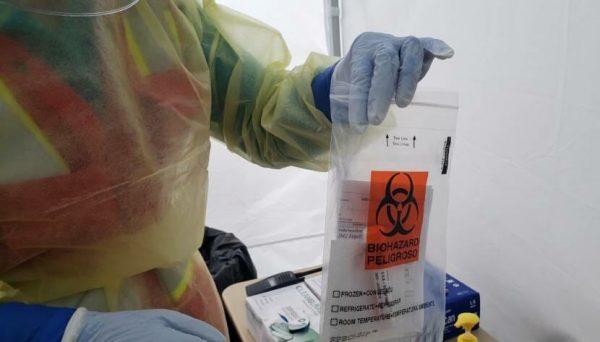 A public health worker in a tent outside Juneau International Airport bags a freshly collected nasal swab for COVID-19 testing.