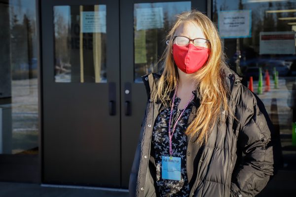 a person stands with a badge and mask on in front of doors