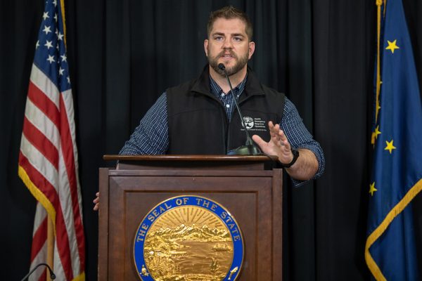 A white man with a mustache and beard speaks at a podidum with a state of Alaska seal