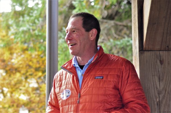 A white man in a orange patagonia jacket standing next to a window