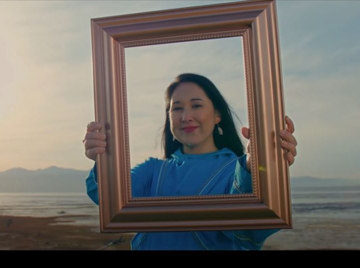 A woman in an anorak holds up a photo frame and looks through it