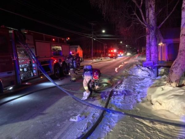 A firefightes leans over a hose on a snowy road next to a fire truck.