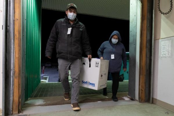 Two people carry a large box into a walk-in freezer.
