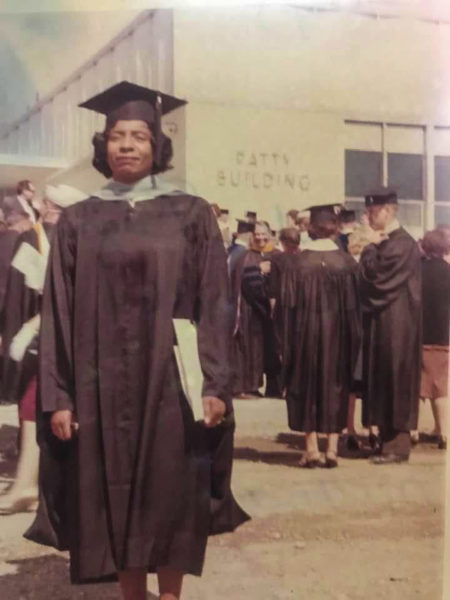 an old photo of a Black woman in a graduation gown in front of a mostly white crowd