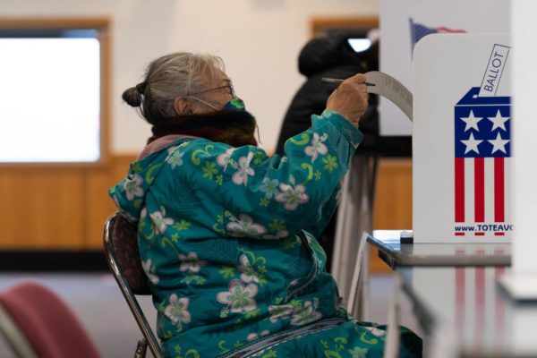 A Bethel woman in a flowery parka and mask reads her ballot.