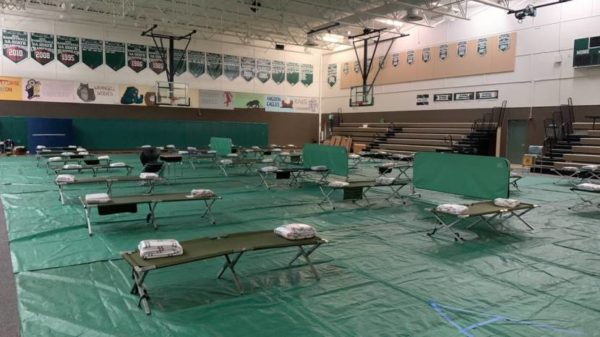 A gym floor covered in tarps and cots for evacuated residents.