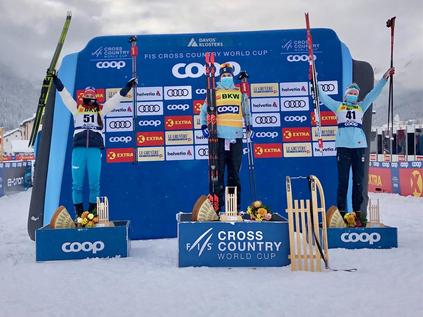 Three women hold up skis on podiums