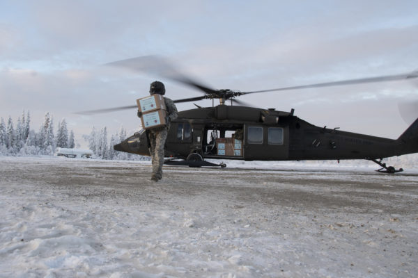 A masked man carries a box on a snoowy ground from his helicopter