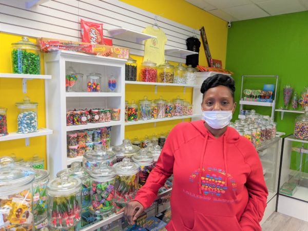 A Black woman stands in front of a counter with medium-sized jars of filled with candy