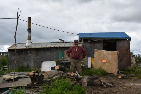 A man stands in front of a modest house