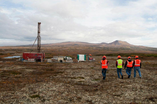 A group of workers in safety vests survey the tundra with a work camp in the background