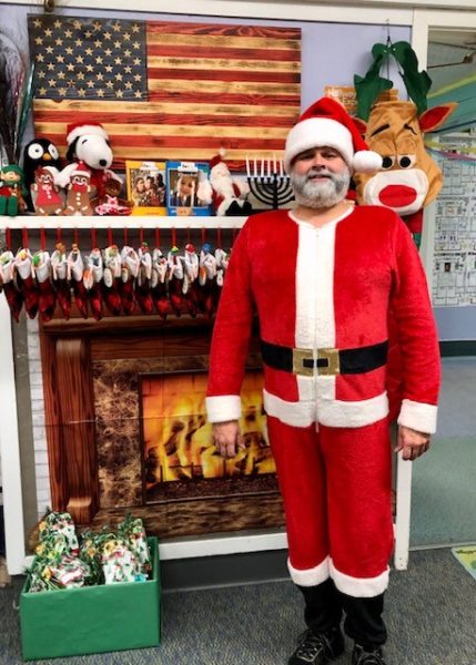 A man dressed up in a santa costume standing in front of a festive fireplace