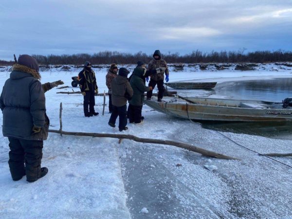People stand around a skiff on some shore ice