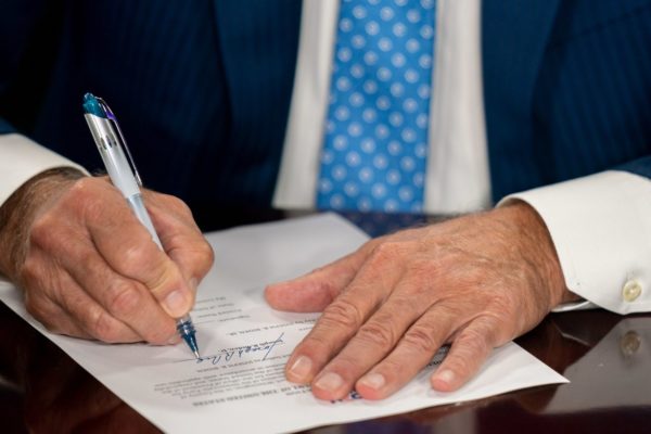 A man's white hands sign a bill