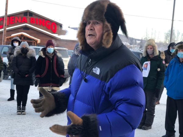 A man in a buffy blue jacket and a fur hat speaks on a winter street
