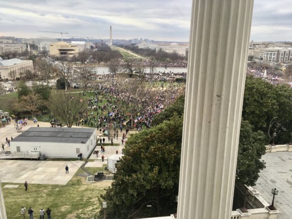 As seen from a window overlooking an empty field, hundreds of protesters gather