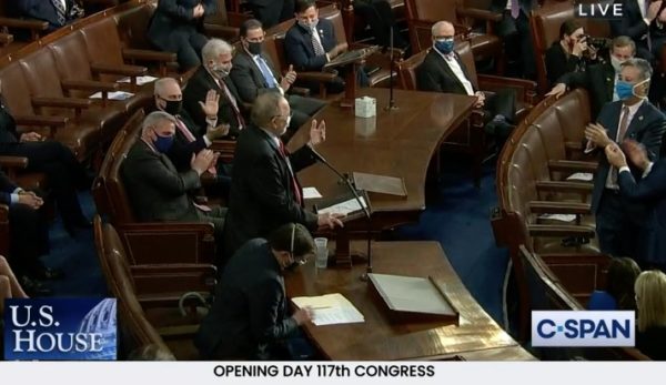 man stands in House chamber, applauded by colleagues