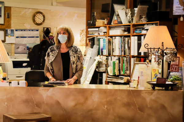 A woman stands behind a counter with a mask on.