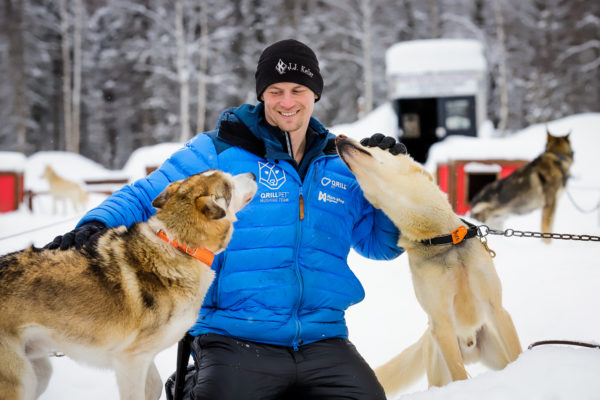 a person in a blue jacket petting his sled dogs