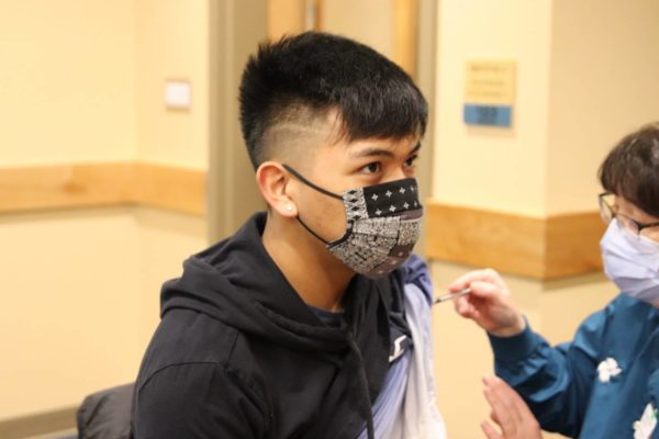 An Alaska native teen with a black mask getting vaccinated
