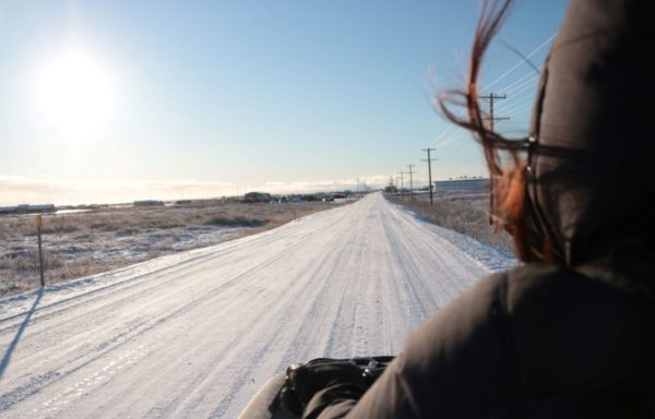 Seen from behind, a woman rides down a snowy straight road