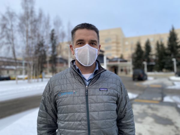 A man stands outside in a jacket and face mask.