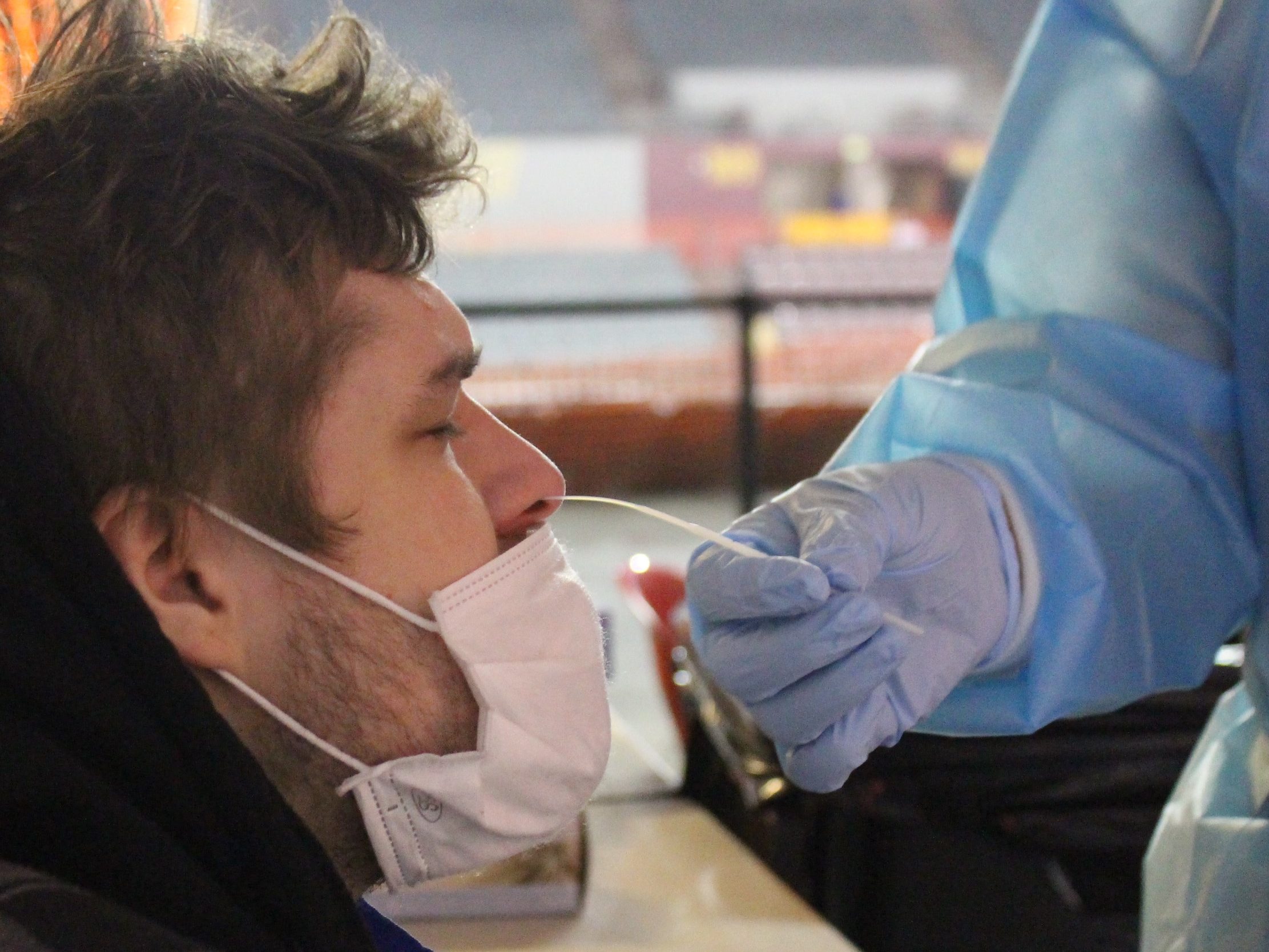 A white man gets his nose swabbed by a person in blue latex gloves 